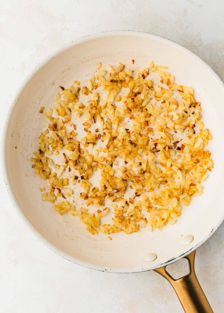 A white pan of sauteed onions on a white counter.