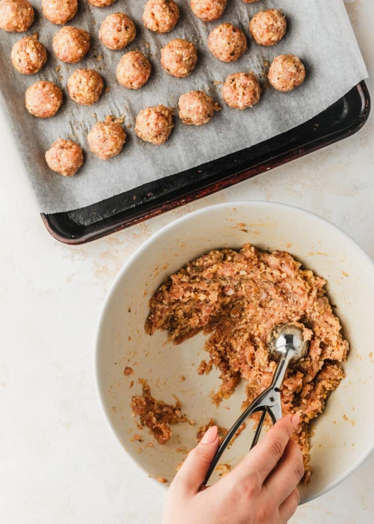 A hand using a scoop to divide meat for air fryer chicken meatballs.