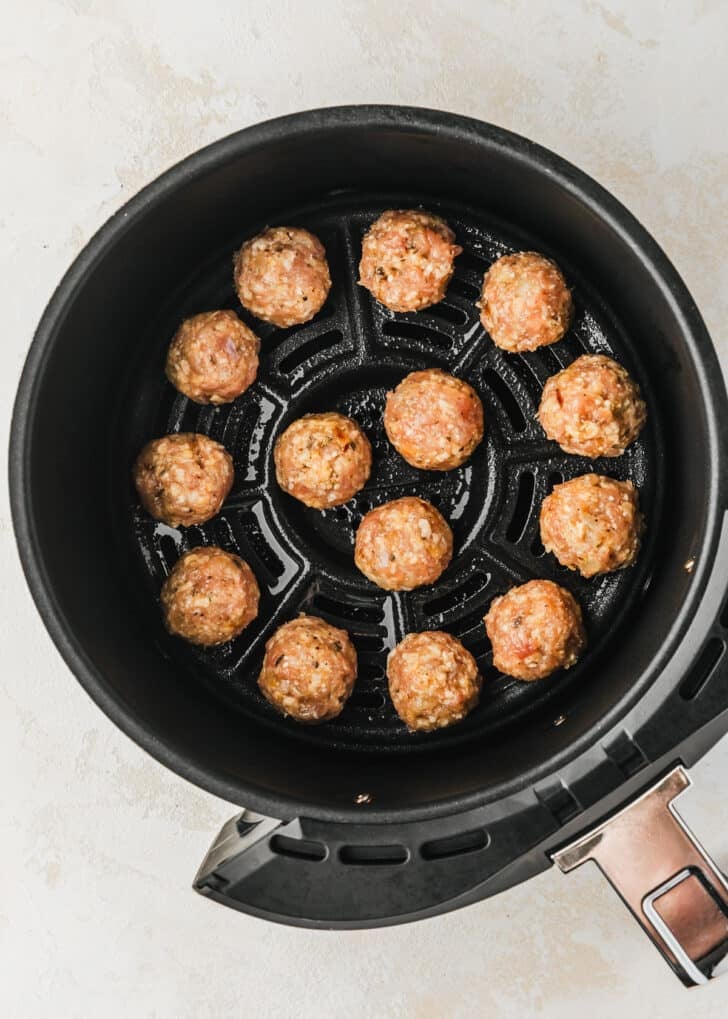 Raw chicken meatballs in an air fryer basket.