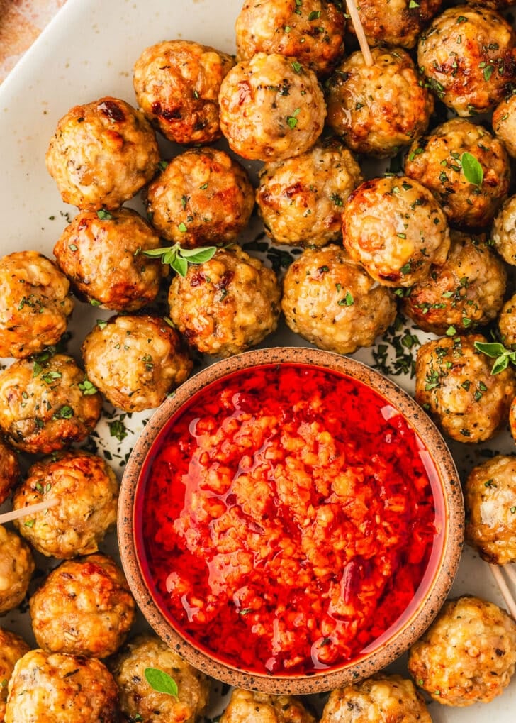 A tray of air fryer chicken meatballs and a brown bowl of red sauce.