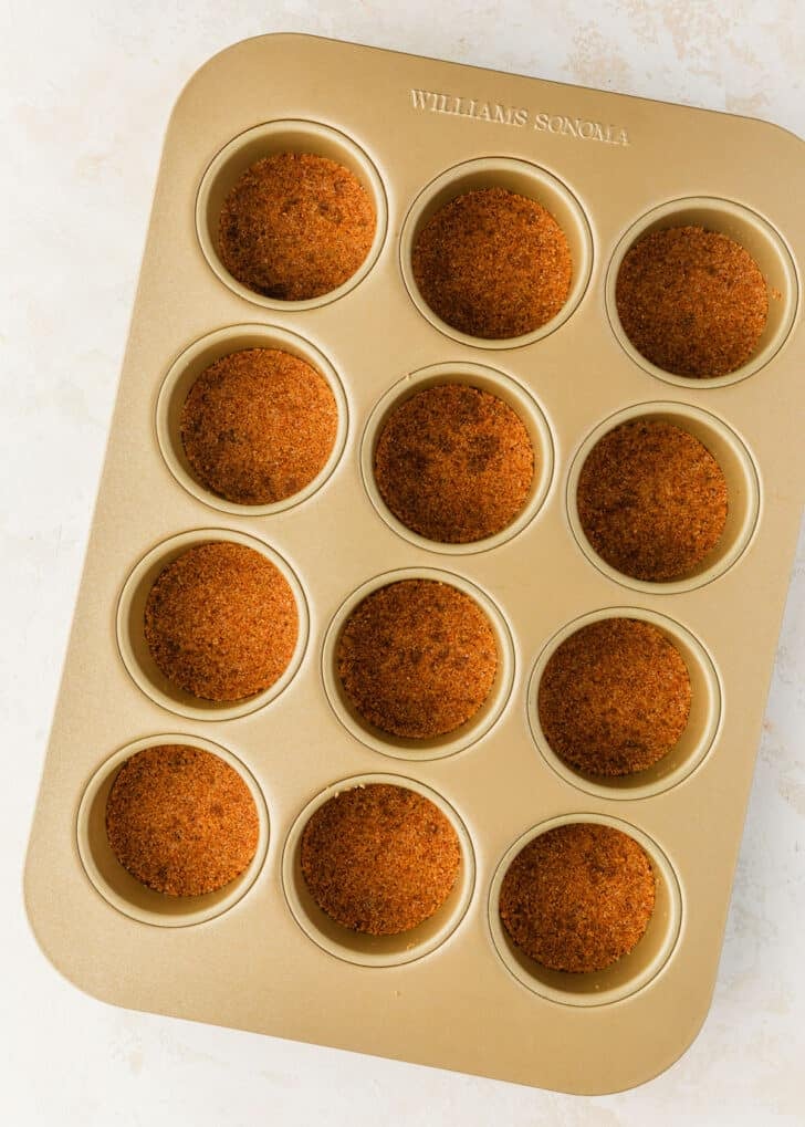 A mini cheesecake pan with graham cracker crusts on a tan counter.