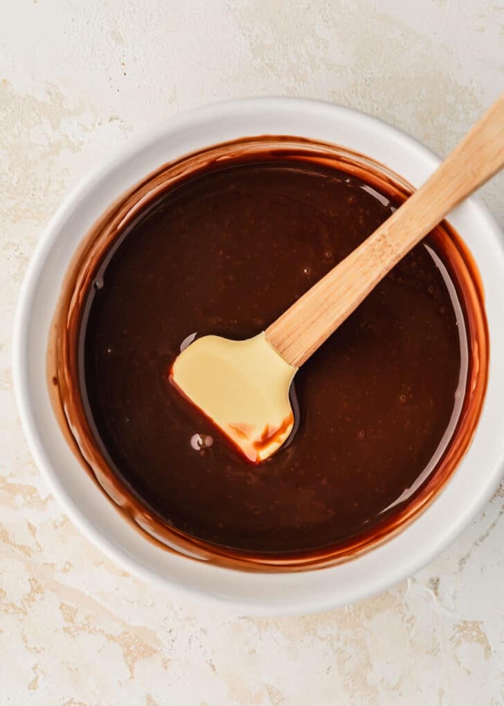 A white bowl of chocolate ganache on a beige table.
