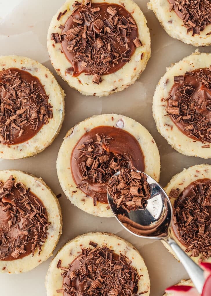 A hand using a spoon to top mini egg cheesecakes with chocolate curls.
