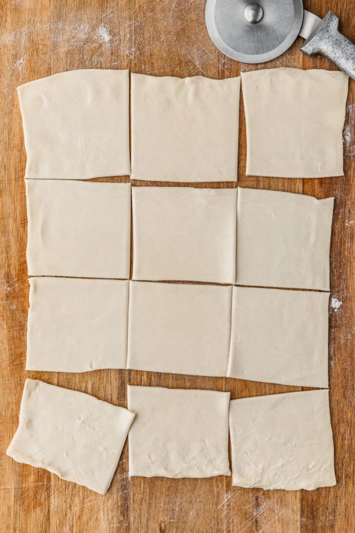 A wooden pastry board topped with 12 puff pastry squares.