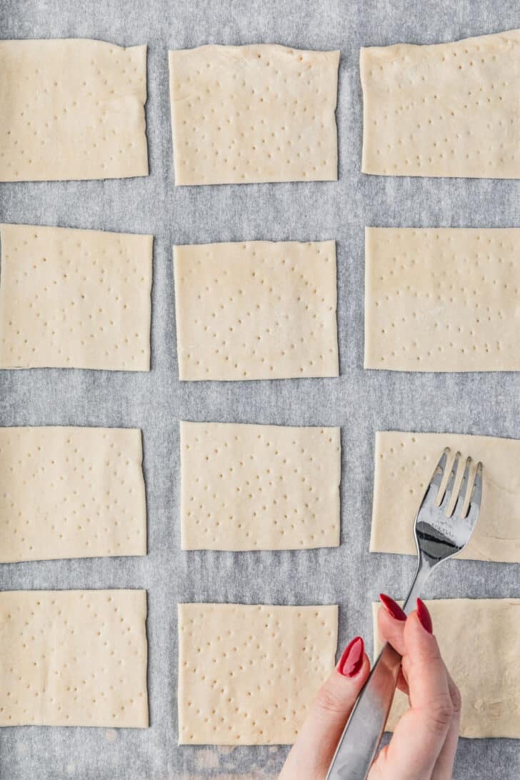 A hand using a fork to dock pastry squares.