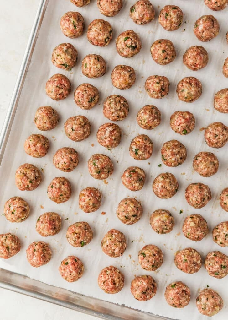 Rows of raw Spanish meatballs on a sheet pan.