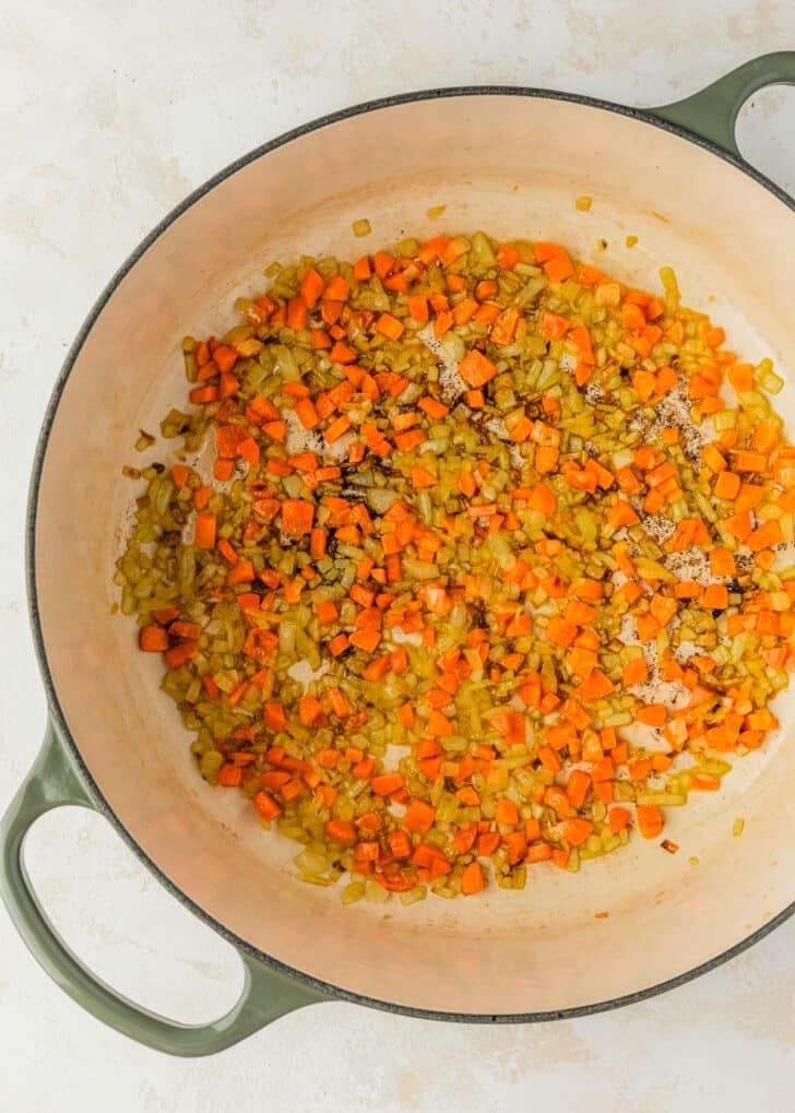 A white pot of sauteed onions and carrots.