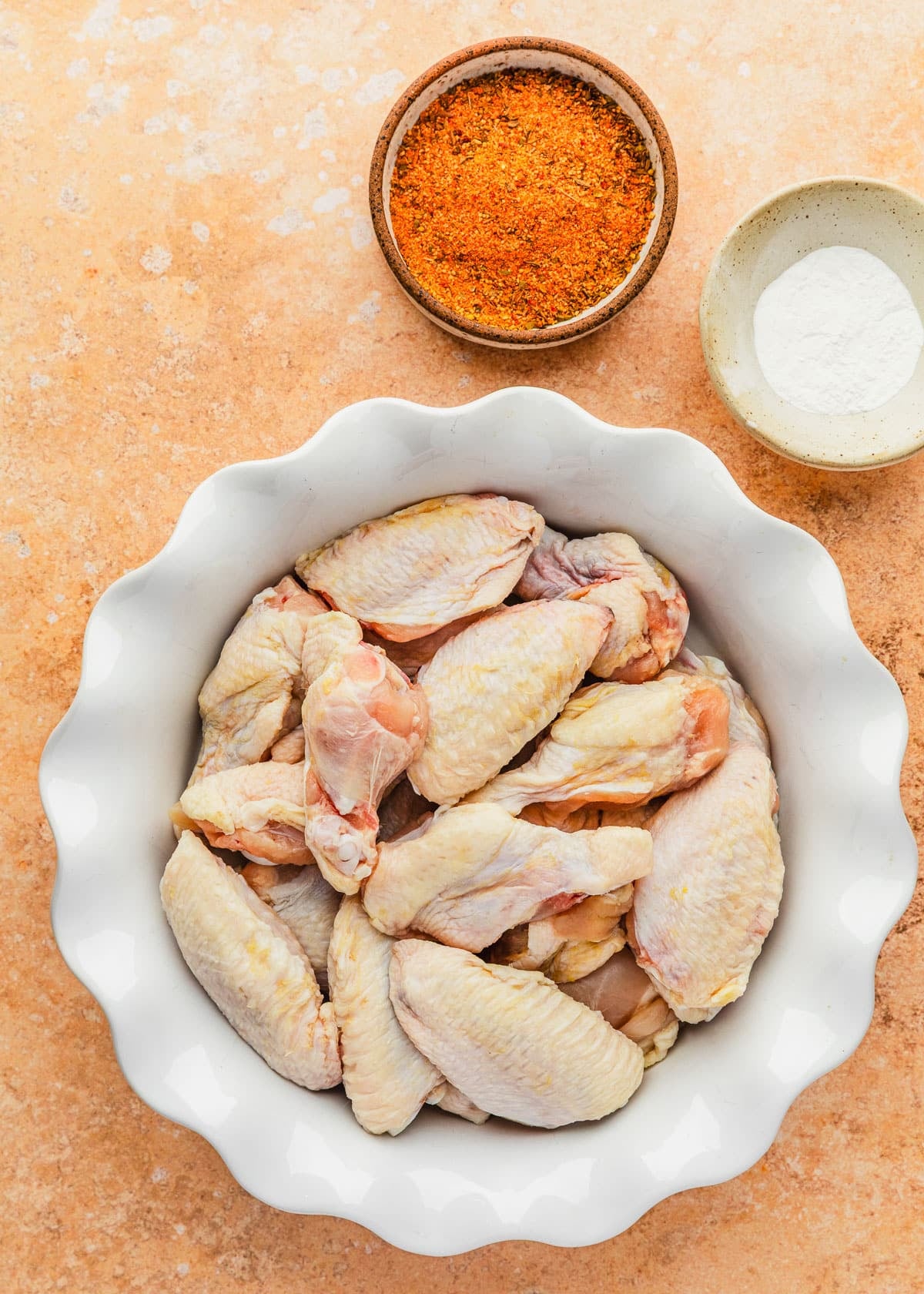White and brown bowls of wings, baking powder, and Cajun seasoning on an orange counter.