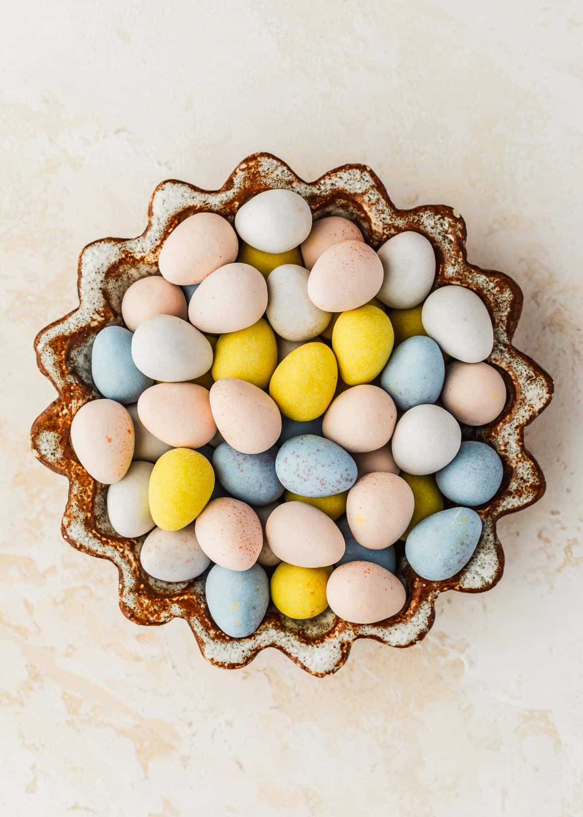 A brown and white bowl of egg candies on a beige counter.