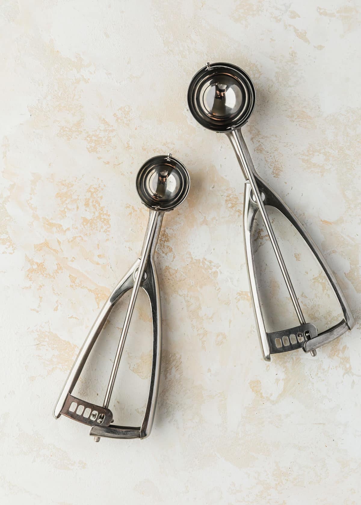 Two cookie scoops on a tan counter.