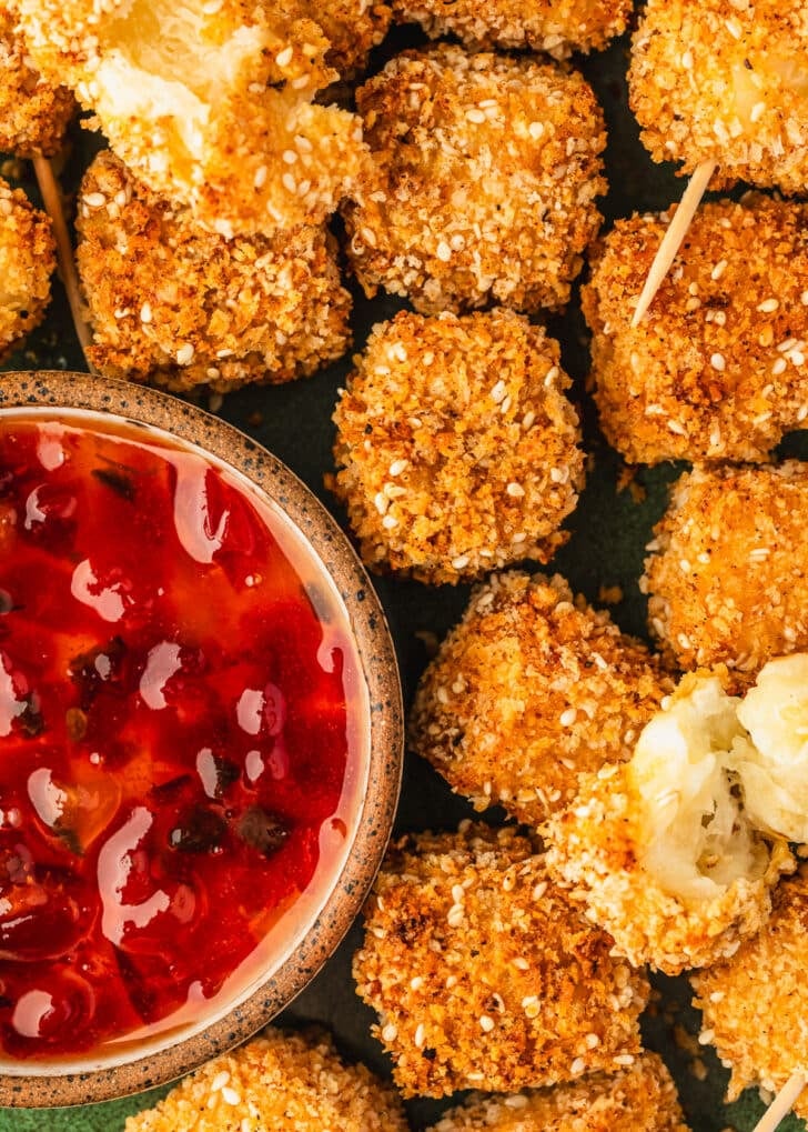 A platter of crispy halloumi cheese bites next to a brown bowl of red pepper jelly.