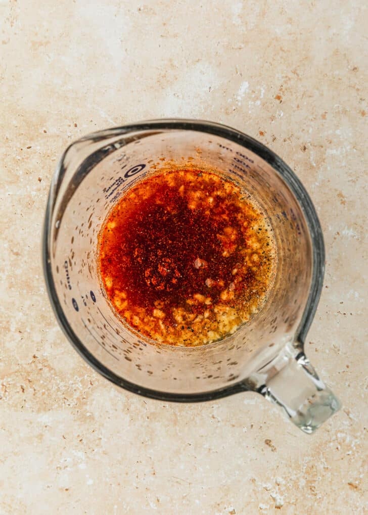 A measuring cup of dressing on a tan counter.