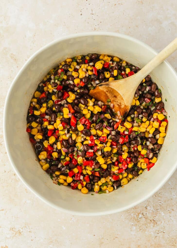 A white bowl of corn and black bean dip on a stone table.