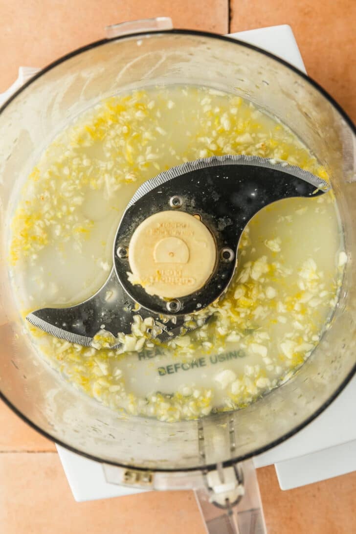 A food processor with blended garlic and lemon juice.
