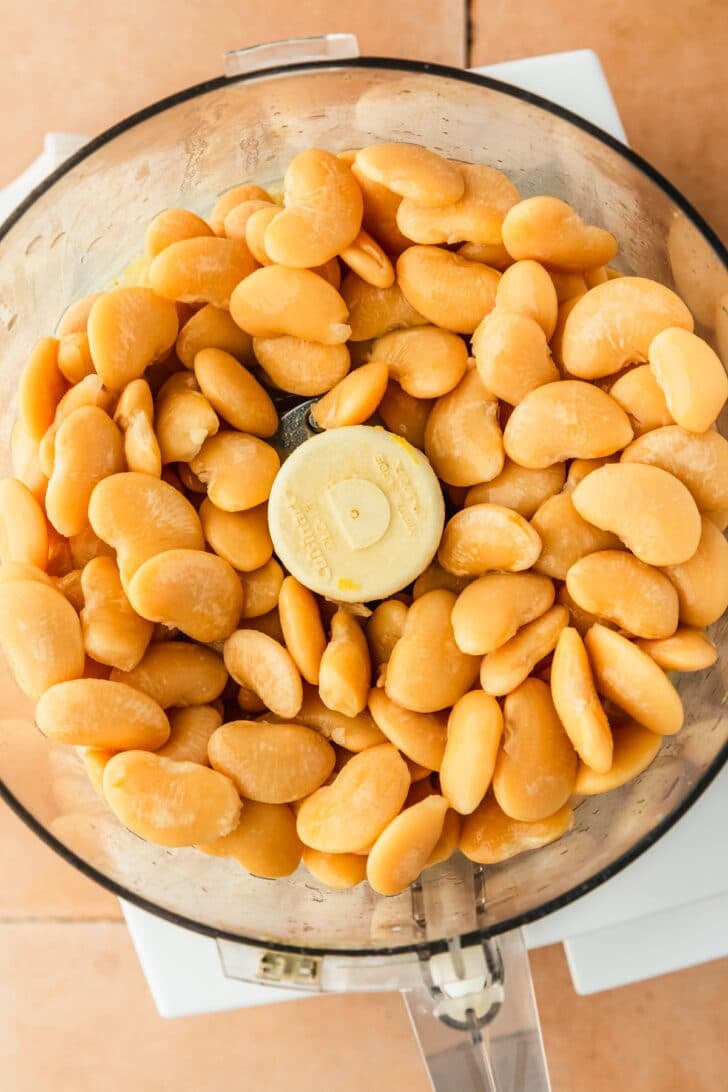 A food processor with butter beans on an orange tile counter.