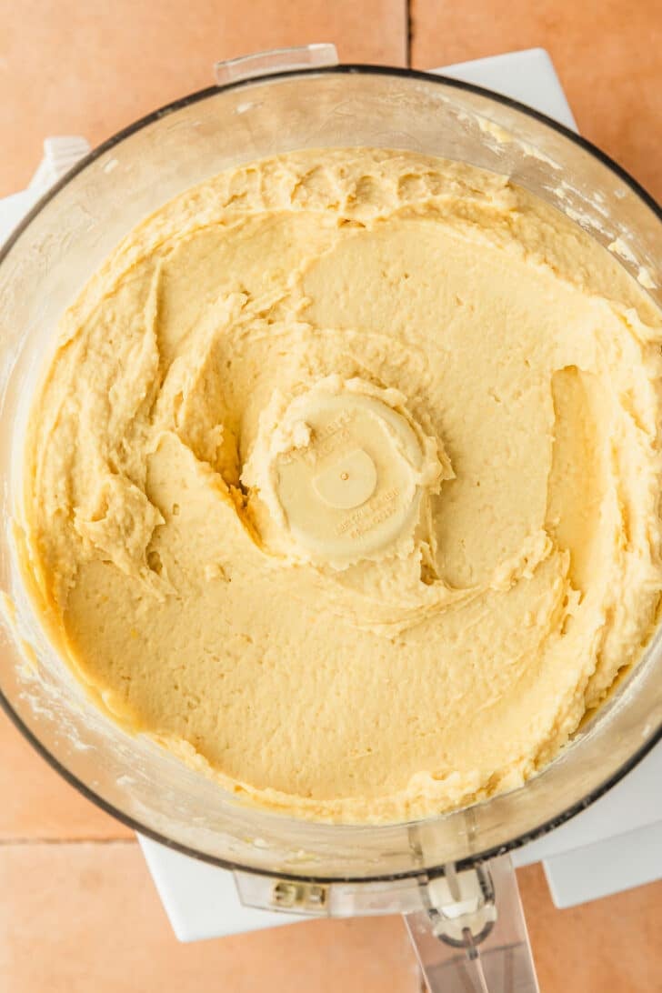 A food processor butter bean dip on an orange tile table.