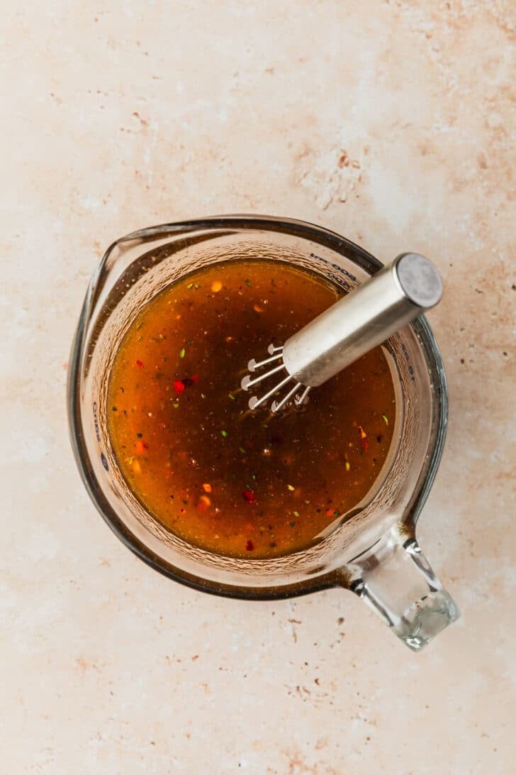 A glass measuring cup with honey, oil, butter, and spices on a tan counter.