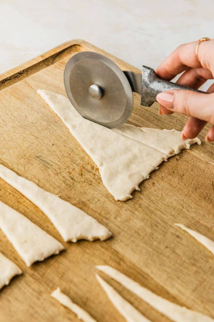 A hand using a pizza cutter to cut rolls on a wood board.
