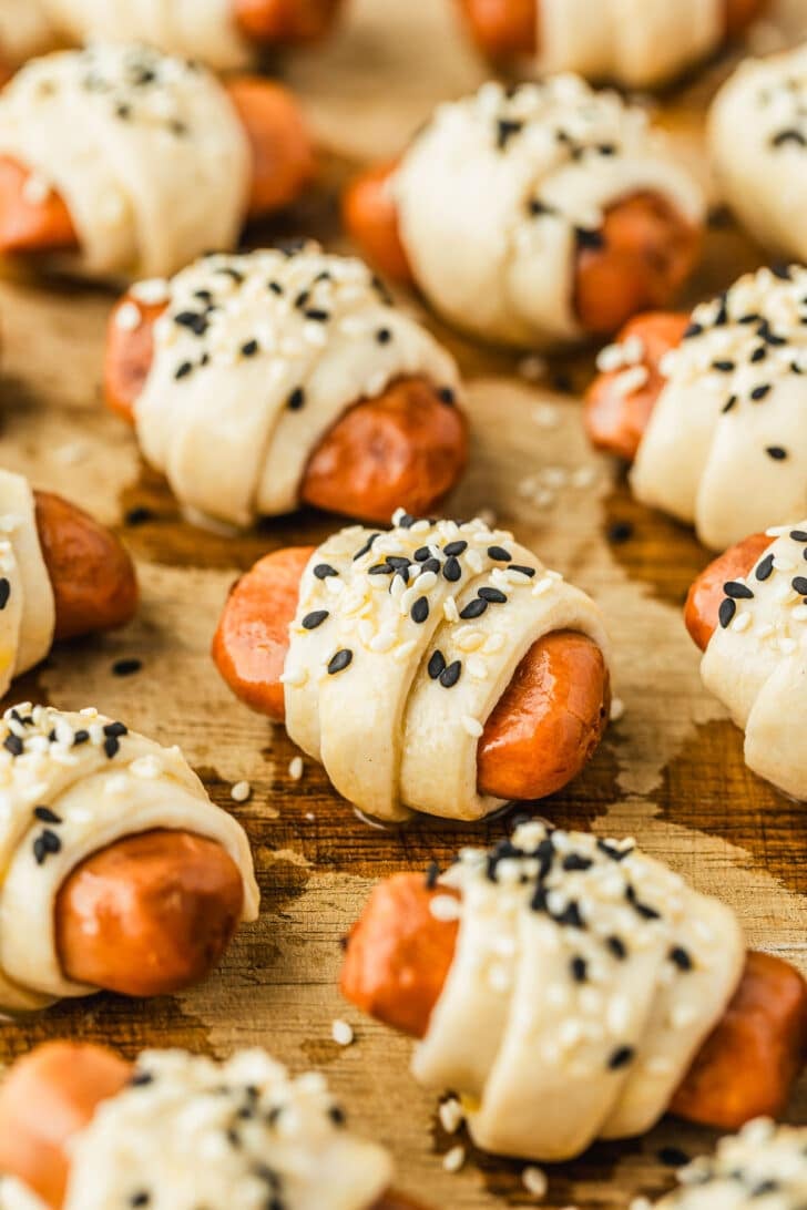 Raw air fryer pigs in a blanket with sesame seeds on a wood board.