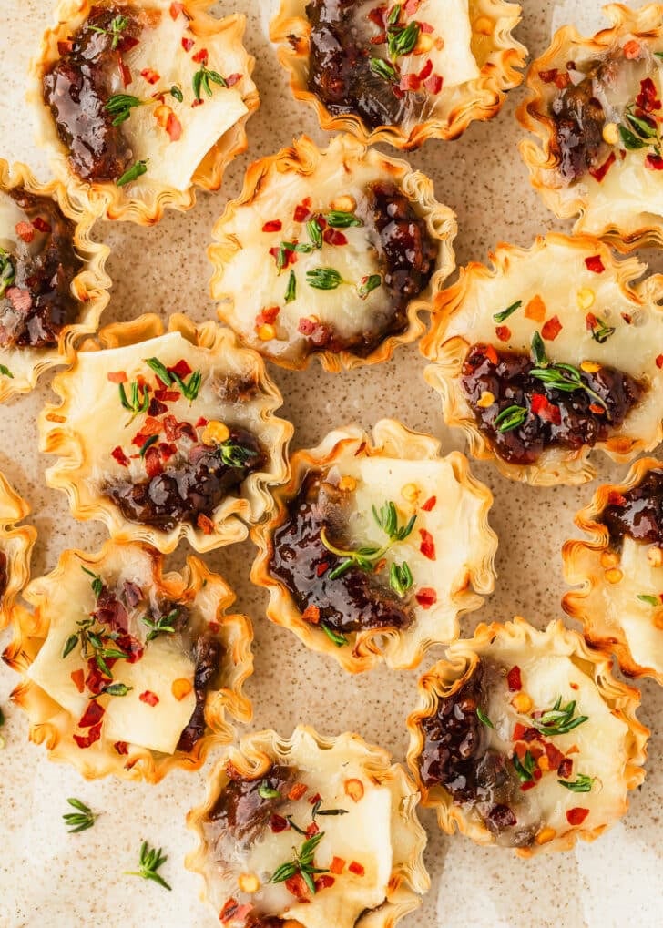 A tan platter of bacon jam and brie phyllo cups with thyme sprigs.