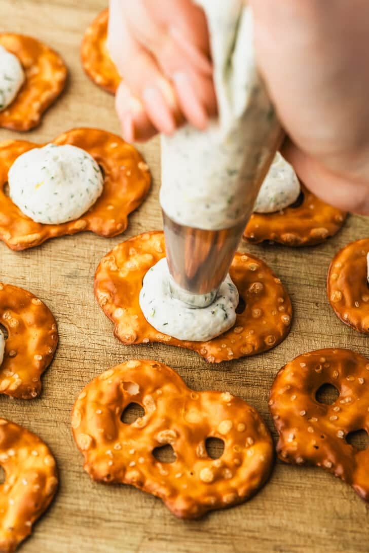 A hand piping cheese filling on pretzel crisps.