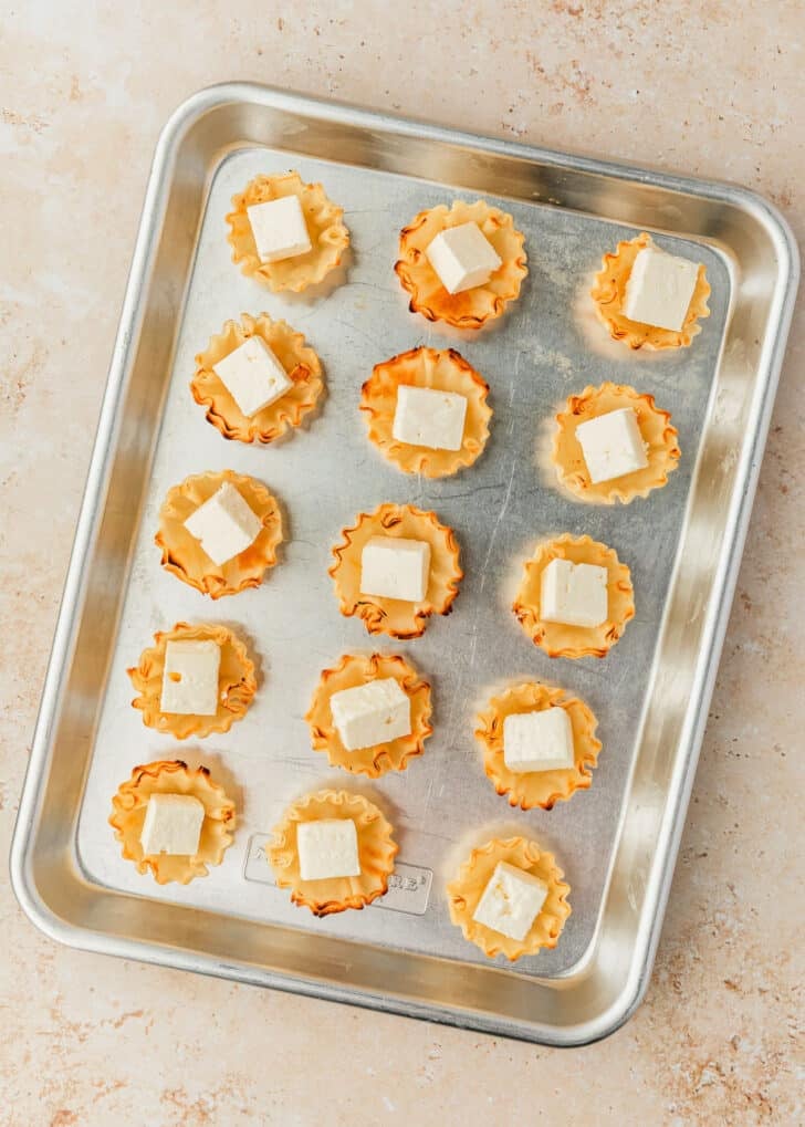 A silver tray of filo shells filled with cheese on a tan counter.
