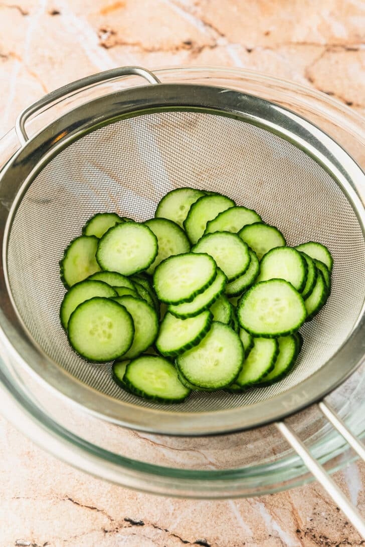 A colander of cucumbers on an orange marble counter.
