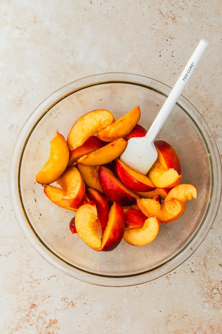 A glass bowl of nectarines on a brown stone counter.