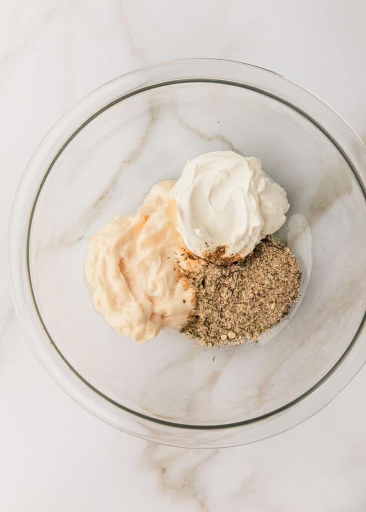 A clear bowl of mayo, sour cream, and seasoning on a white marble counter.