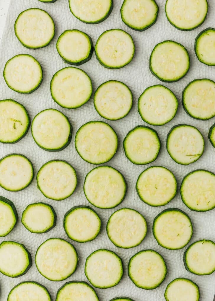 Rows of sliced zucchini coins topped with salt on paper towels.