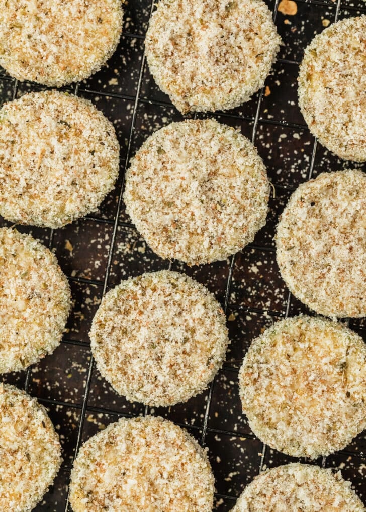 Rows of breaded zucchini for fried zucchini on a wire rack.