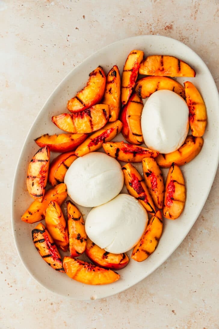 A white platter of grilled peaches and burrata on a tan counter.