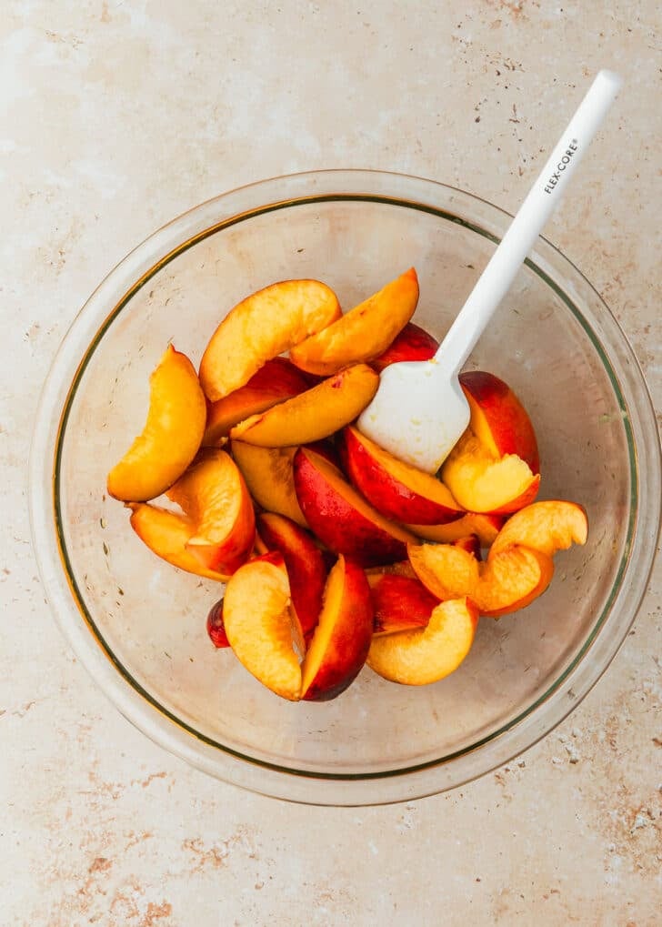 A clear bowl of peach slices on a brown counter.