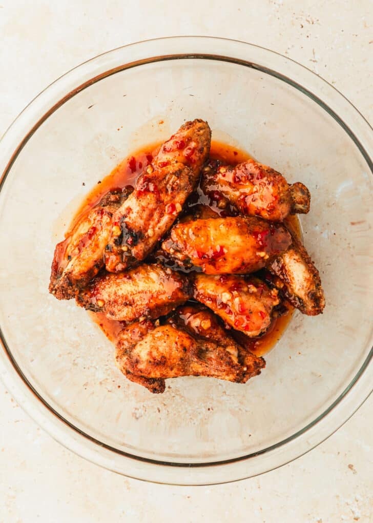 A clear bowl of sweet chili chicken wings on a tan counter.