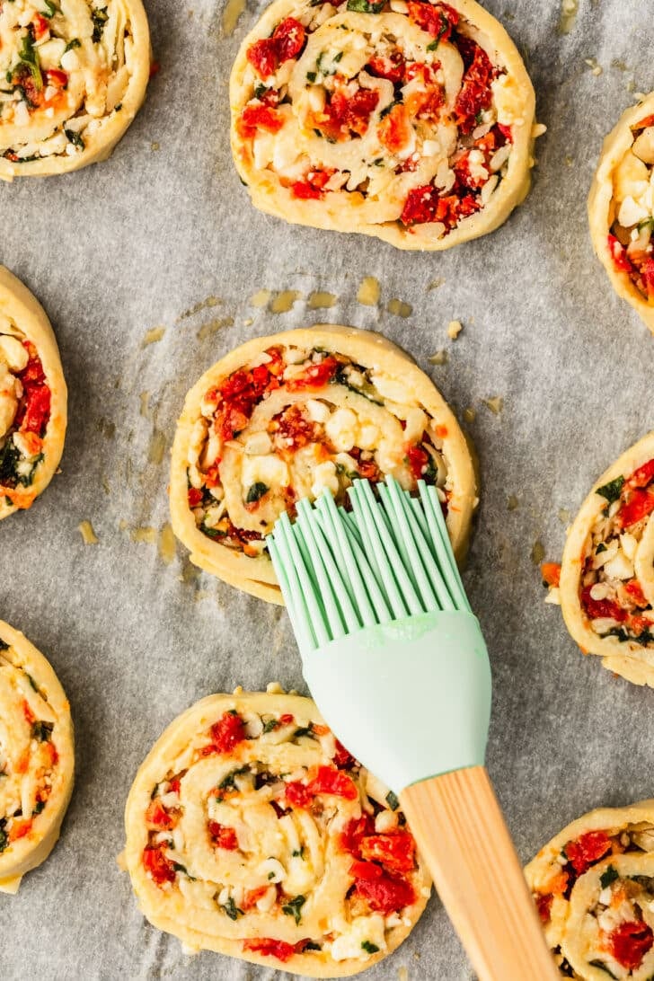 A pastry brush brushing egg wash on pinwheels.