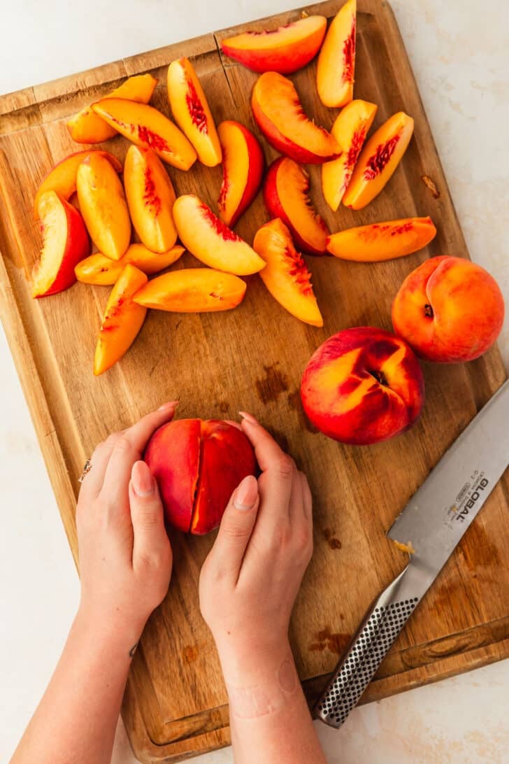 Hands pulling apart a peach on a wood board.