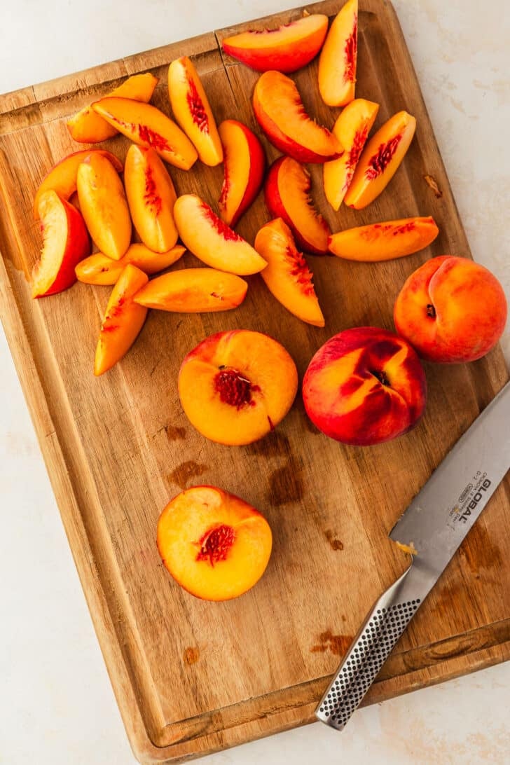 A halved peach on a wood board of sliced peaches.