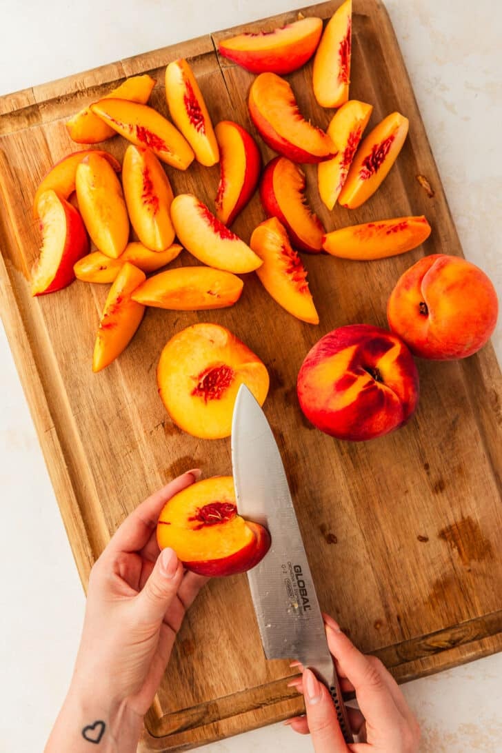 A hand using a knife to slice a peach around the pit.
