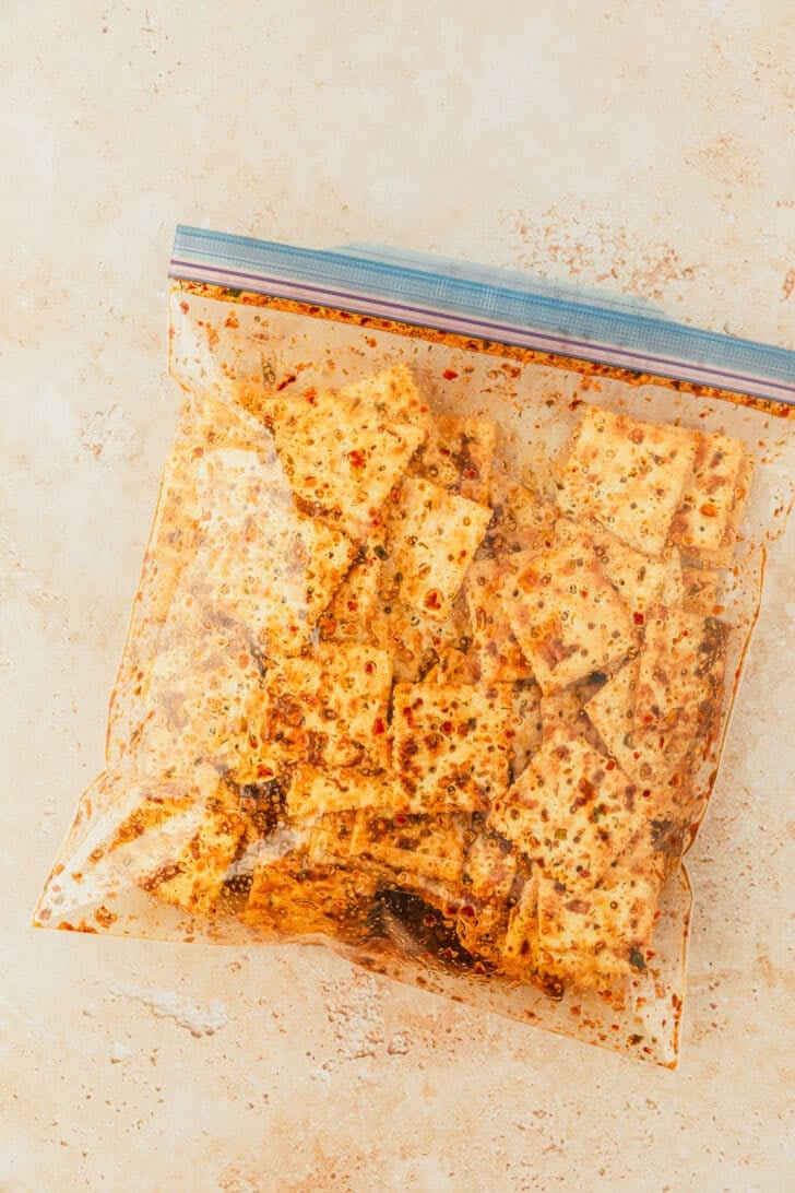 A baggie of oil, spices, and Saltines on a tan counter.