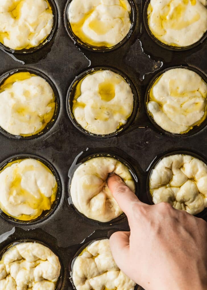 A hand poking dough in a muffin tin for focaccia muffins.