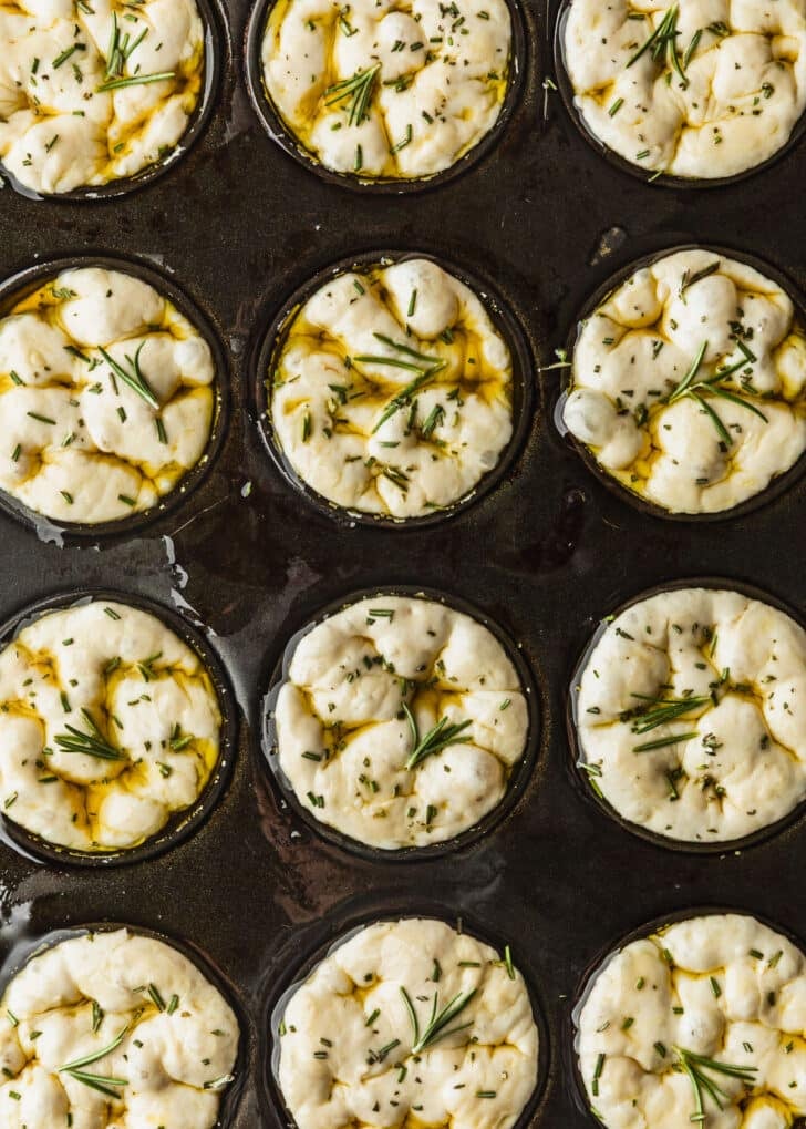 A pan of raw focaccia muffins with rosemary.