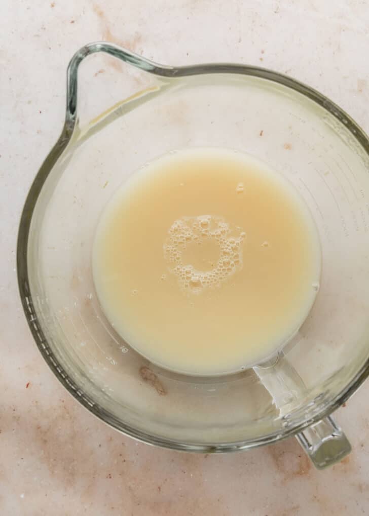 A clear mixing bowl of mixed water and yeast on a tan counter.