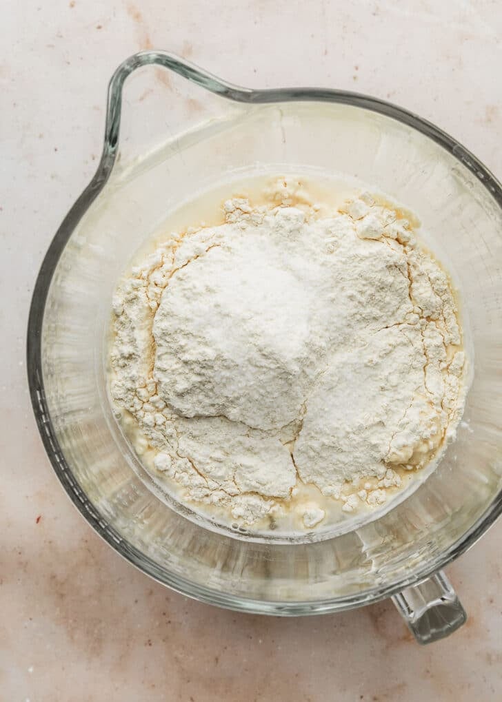 A clear mixing bowl with yeast and bread flour on a tan table.