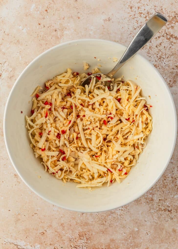A white bowl of cheese, garlic, and chopped peppers on a tan counter.