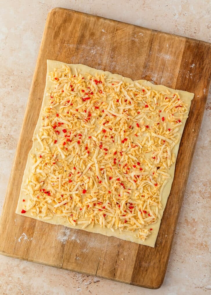 Puff pastry covered with cheese on a wood board.
