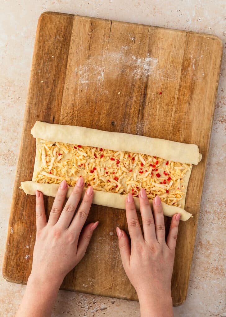 Hands rolling vampire slayer garlic cheddar palmiers on a wood board.