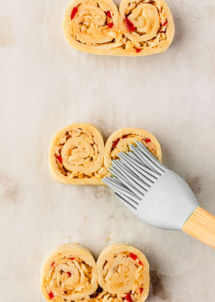 A pastry brush brushing garlic cheddar palmiers with egg wash.