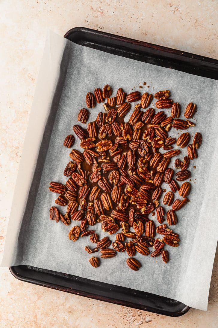 A sheet pan with pecans and maple syrup.