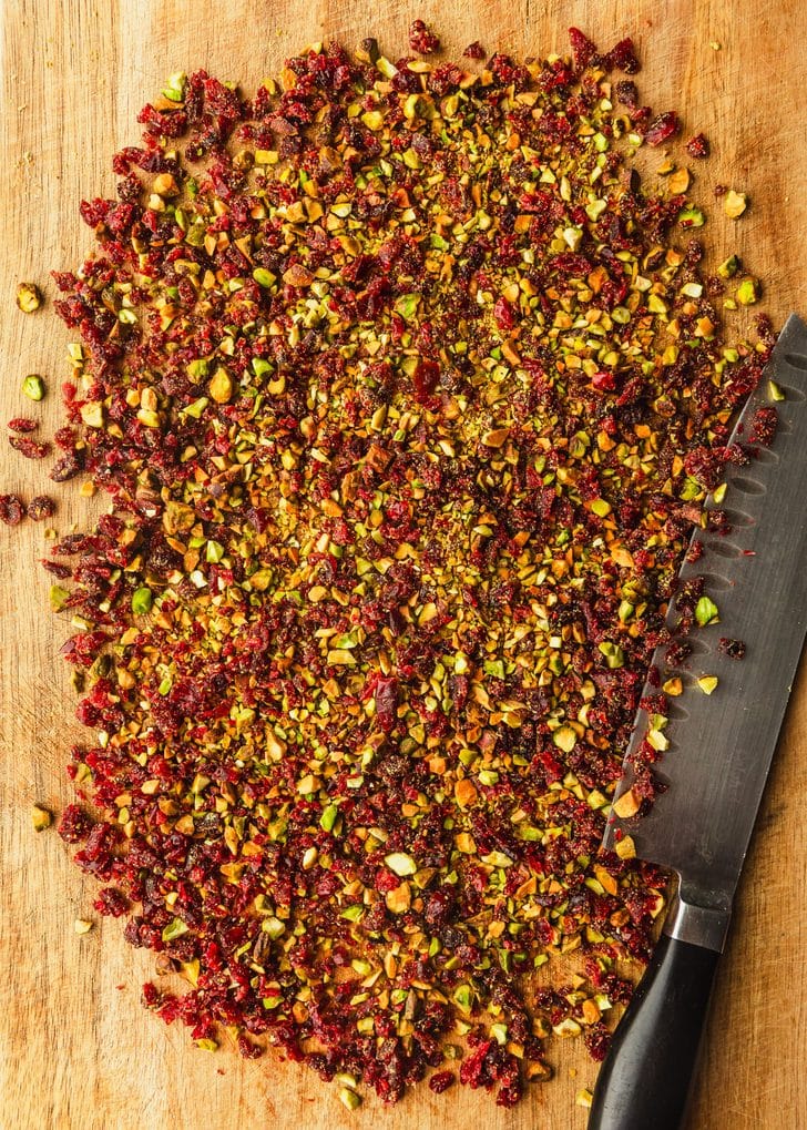 Chopped cranberries and pistachios on a wood board.