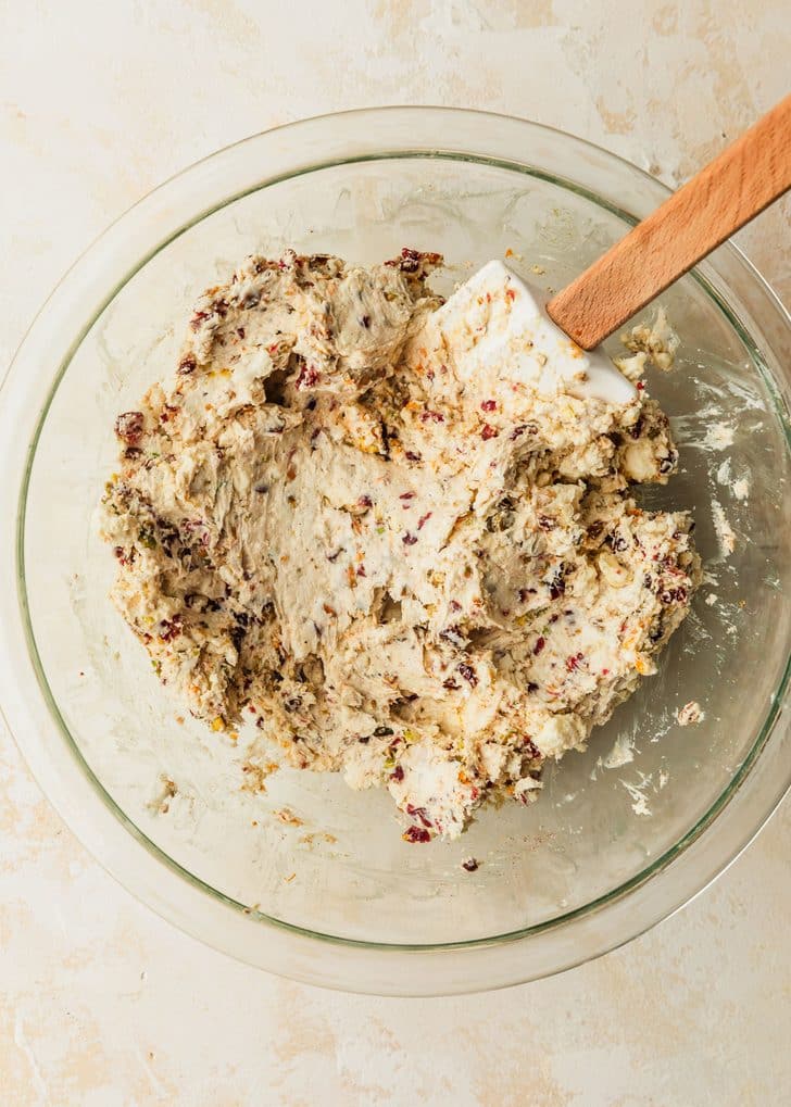 A clear bowl of cream cheese with seasonings on a tan counter.